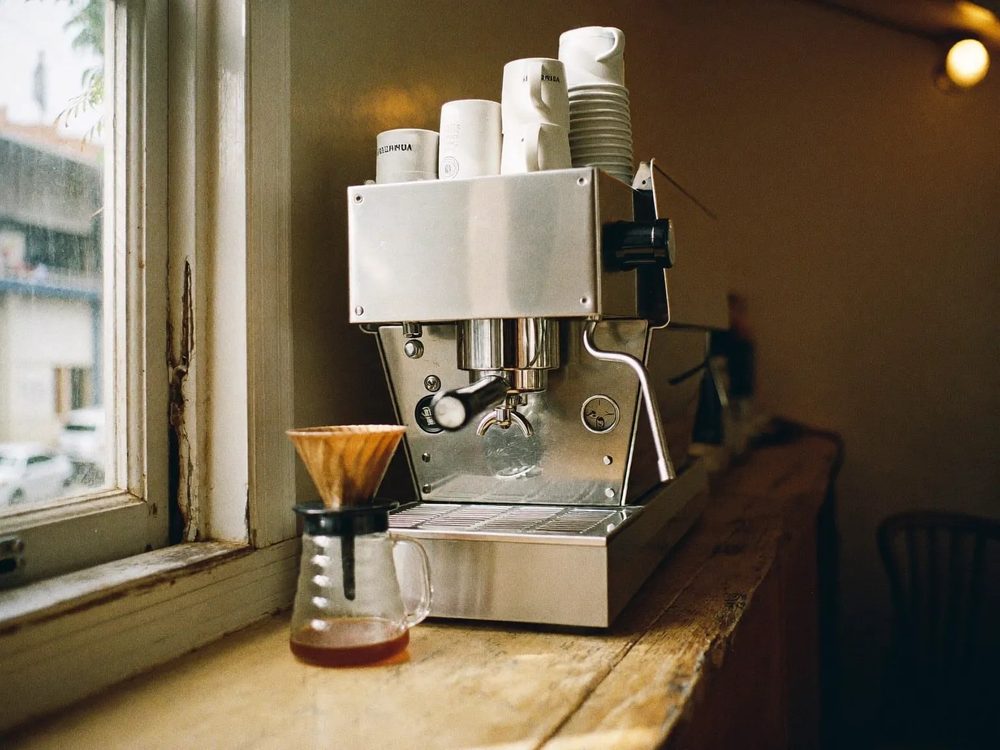 An espresso machine and a stack of white cups on a cafe counter in warm side light